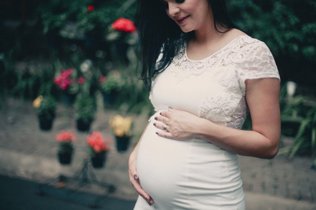 Close up photo of pregnant woman in white dress holding her stomach